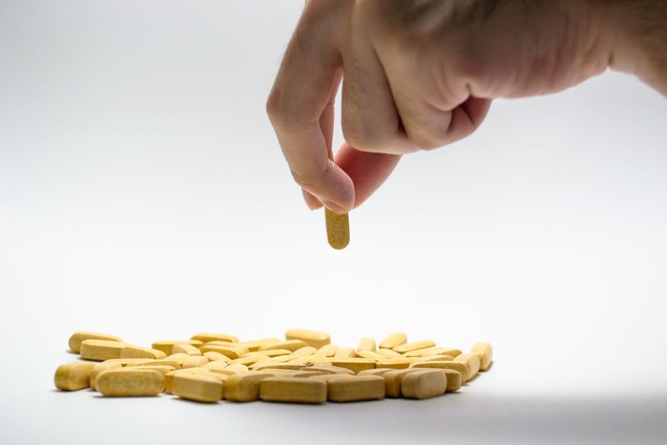 Close-up of a hand holding a supplement capsule above a small pile of capsules